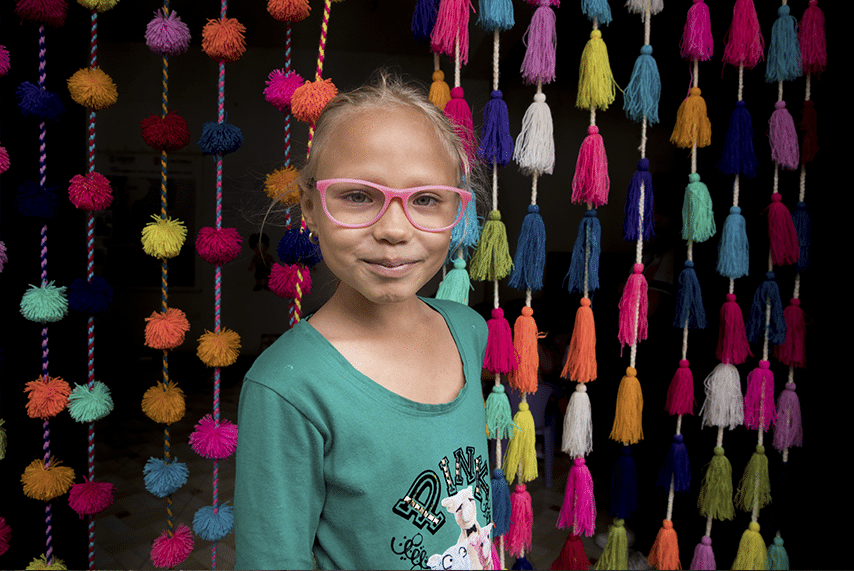 Sofia standing in front of a colorful curtain at home and smiling